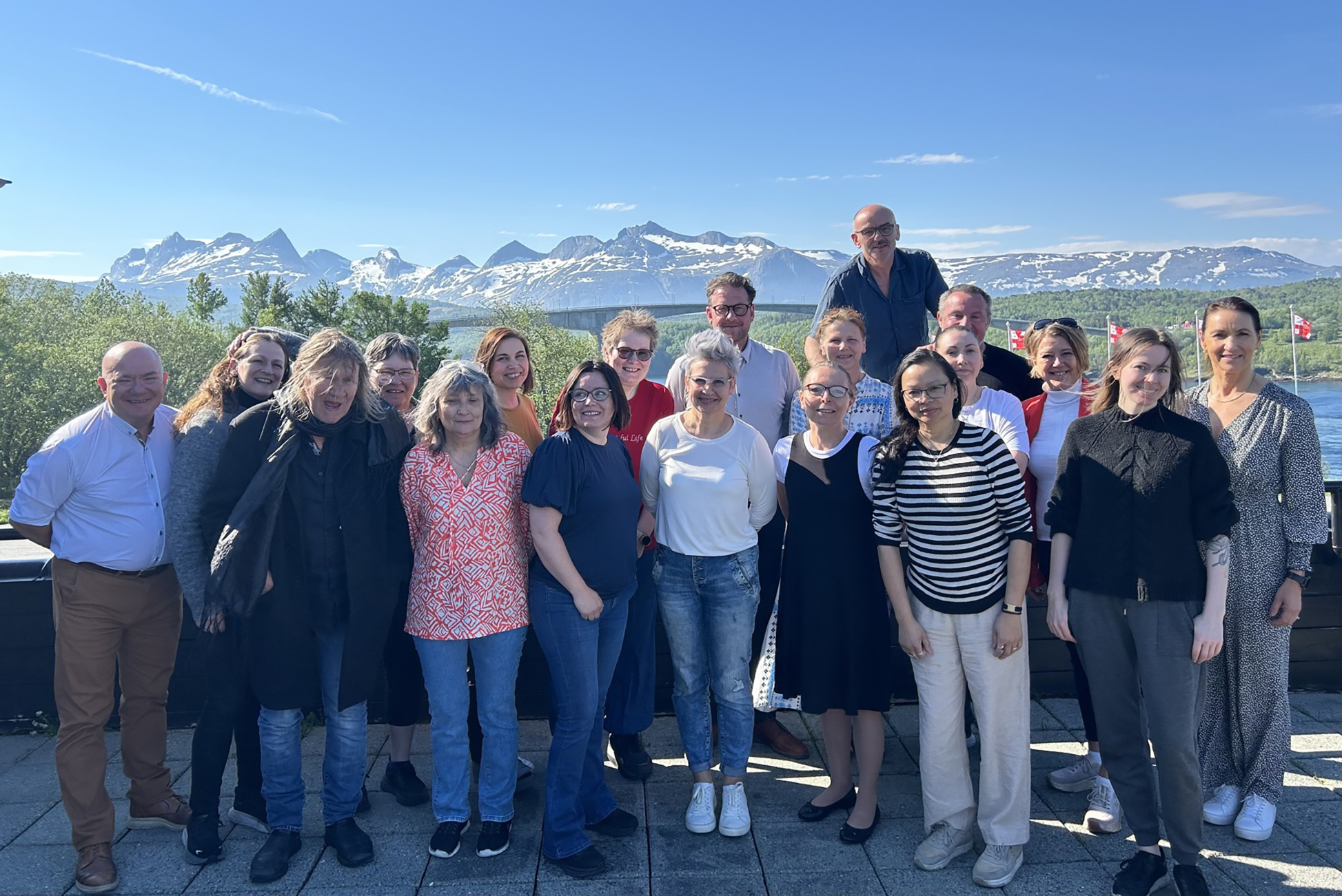 Et oppstilt gruppebilde av 19 personer. Blå himmel og fjell i bakgrunnen.